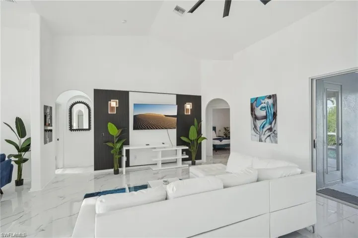 Living area with marble finish floor, high vaulted ceiling, arched walkways, and ceiling fan
