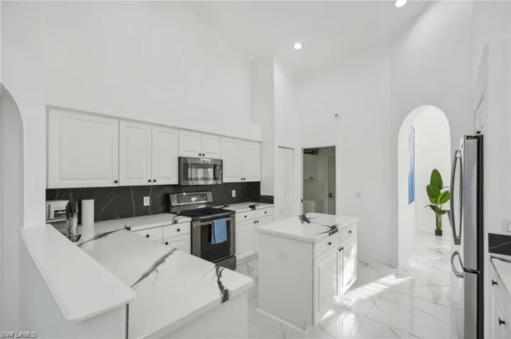 Kitchen featuring stainless steel appliances, a center island, marble finish floor, arched walkways, and white cabinets
