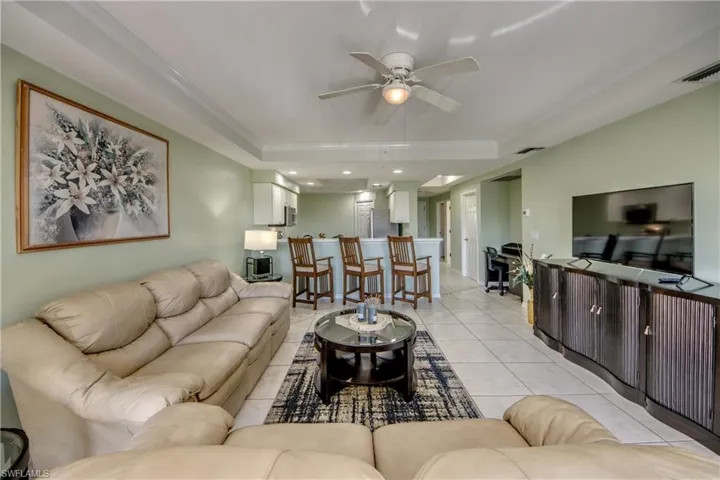 Living room with light tile patterned floors, a raised ceiling, ceiling fan, and ornamental molding