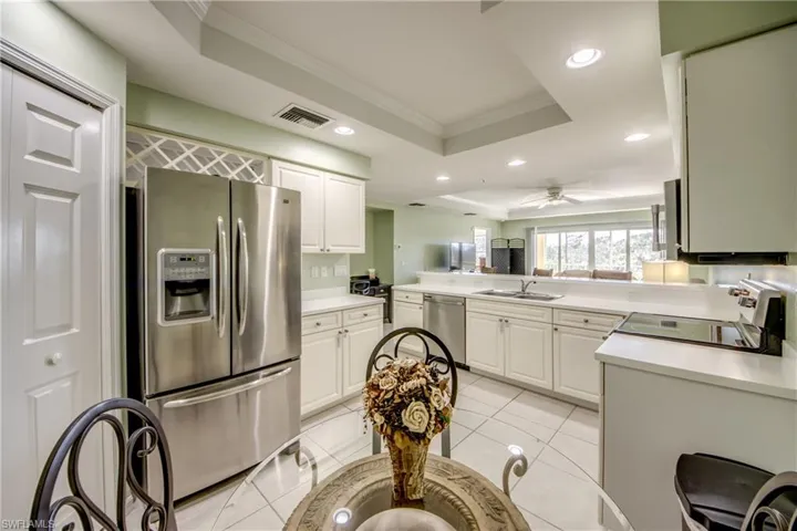 Kitchen featuring a raised ceiling, kitchen peninsula, white cabinetry, and appliances with stainless steel finishes