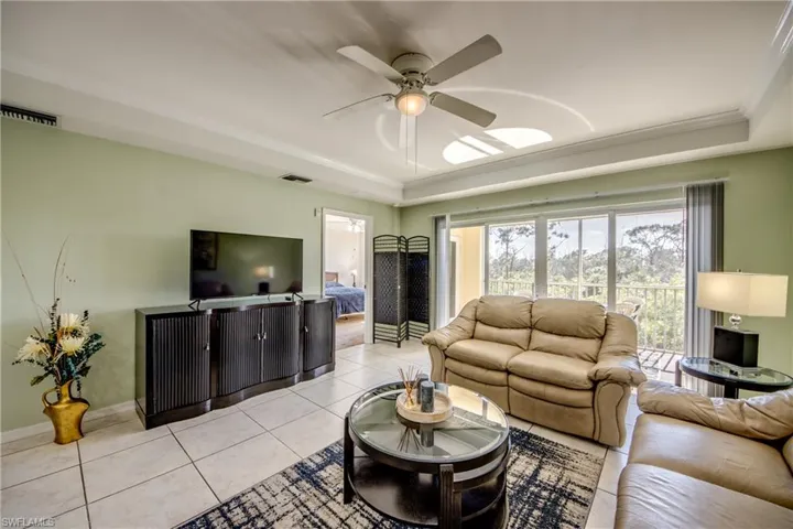 Living room with a raised ceiling, ceiling fan, light tile patterned floors, and ornamental molding