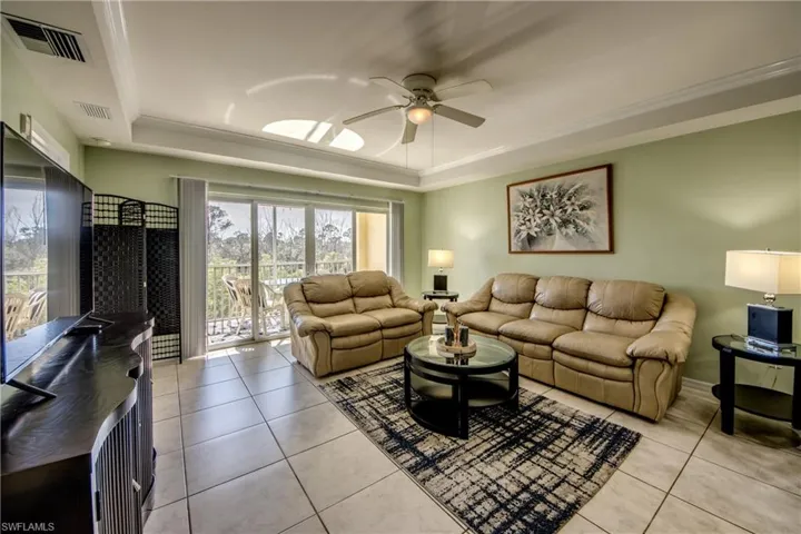 Living room with a raised ceiling, ceiling fan, crown molding, and light tile patterned flooring