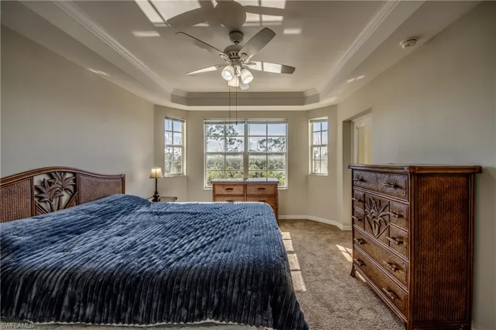 Bedroom featuring a raised ceiling, ceiling fan, light carpet, and ornamental molding