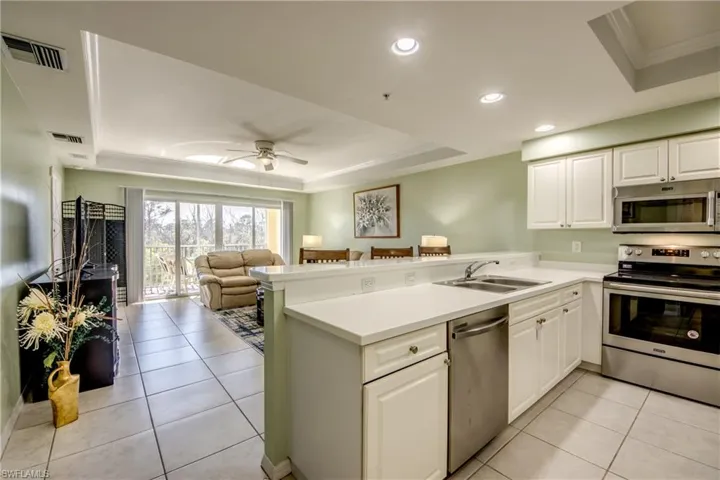 Kitchen featuring a raised ceiling, kitchen peninsula, white cabinets, and stainless steel appliances
