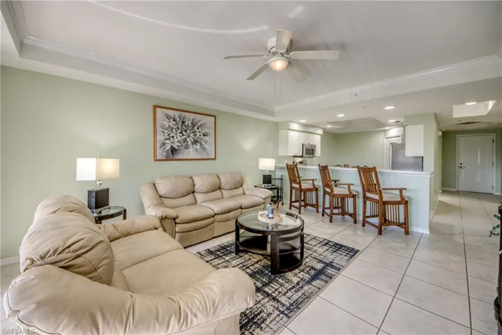 Living room with a tray ceiling, ceiling fan, light tile patterned floors, and ornamental molding