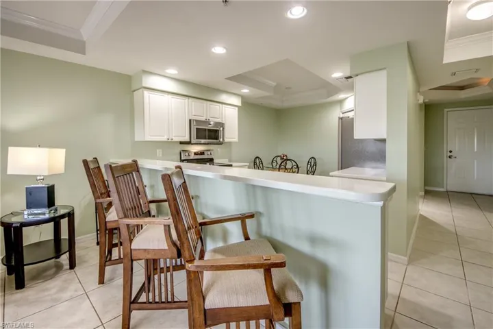 Kitchen featuring kitchen peninsula, appliances with stainless steel finishes, a tray ceiling, crown molding, and white cabinets