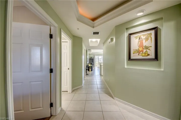 Hallway with a raised ceiling, crown molding, and light tile patterned floors