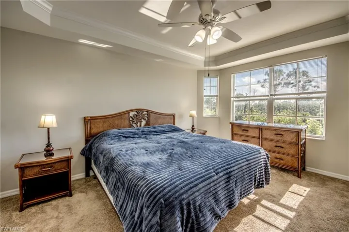 Carpeted bedroom with ceiling fan, a raised ceiling, and ornamental molding