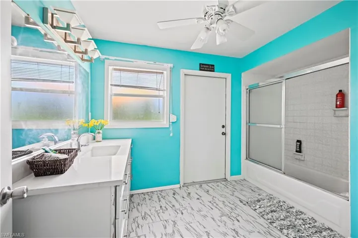 Bathroom with bath / shower combo with glass door, vanity, and ceiling fan