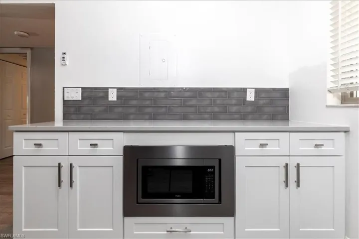 Kitchen featuring decorative backsplash, stainless steel microwave, and white cabinets