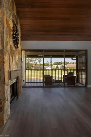 Unfurnished living room featuring dark hardwood / wood-style flooring, a stone fireplace, and wood ceiling