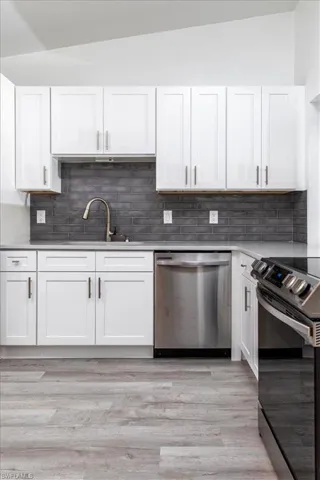 Kitchen featuring white cabinetry, dishwasher, electric range, and lofted ceiling