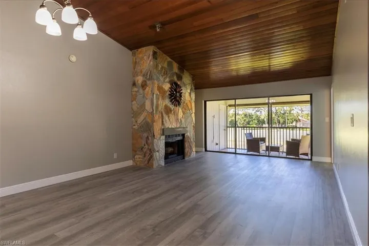 Unfurnished living room featuring hardwood / wood-style flooring, high vaulted ceiling, wooden ceiling, a notable chandelier, and a stone fireplace