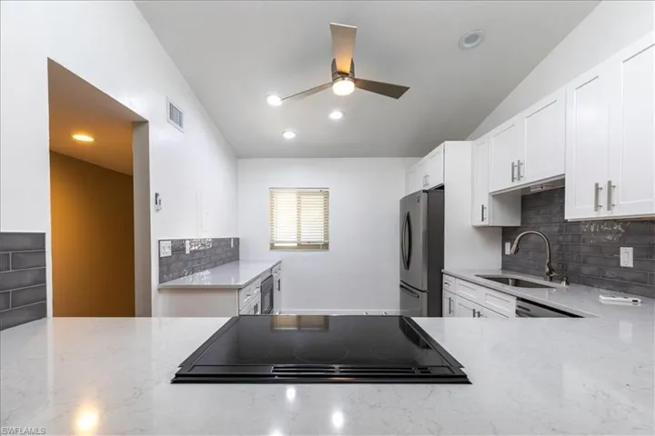Kitchen with stainless steel fridge, light stone counters, black electric cooktop, sink, and white cabinets