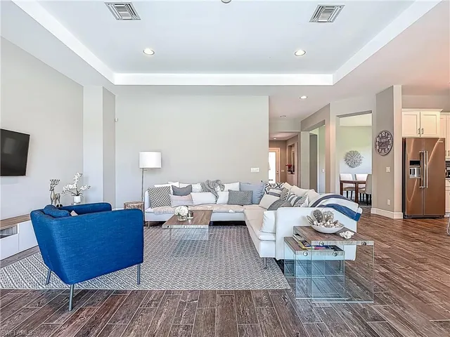 Living area featuring dark wood-style flooring, a raised ceiling, recessed lighting, and baseboards