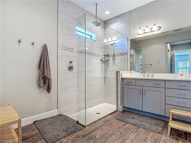 Full bath featuring vanity, wood finished floors, a tile shower, and recessed lighting