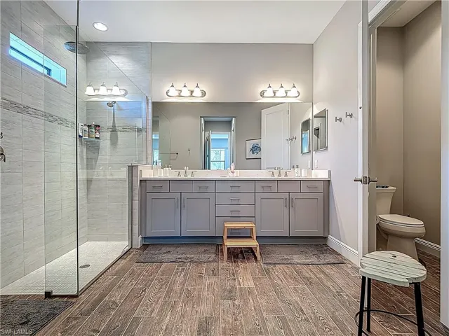 Full bathroom featuring wood finished floors, double vanity, a shower stall, healthy amount of natural light, and recessed lighting