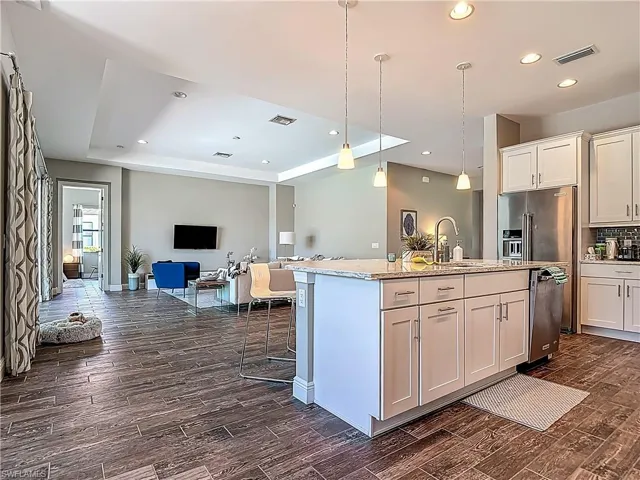 Kitchen featuring a sink, a tray ceiling, dark wood finished floors, open floor plan, and a center island with sink