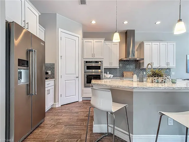 Kitchen with stainless steel appliances, wall chimney exhaust hood, dark wood-style flooring, a kitchen breakfast bar, and backsplash
