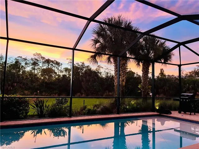 Pool at dusk with glass enclosure, an outdoor pool, a grill, and a patio