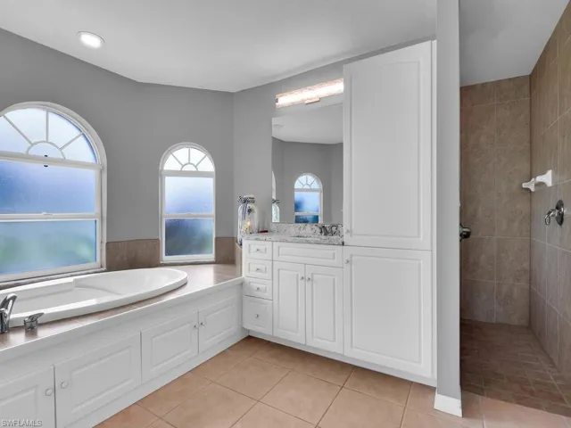 Full bath featuring vanity, light tile patterned floors, a bath, walk in shower, and tile walls