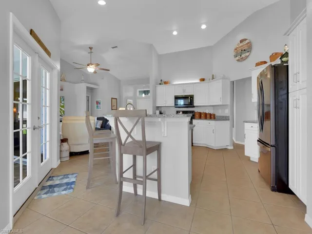 Kitchen with a kitchen bar, light tile patterned floors, stainless steel appliances, white cabinets, and a center island with sink