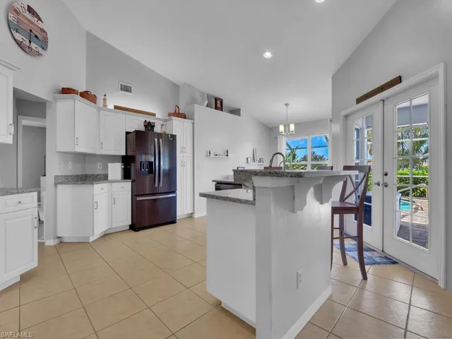 Kitchen featuring stainless steel fridge with ice dispenser, light tile patterned flooring, french doors, a center island with sink, and a breakfast bar area