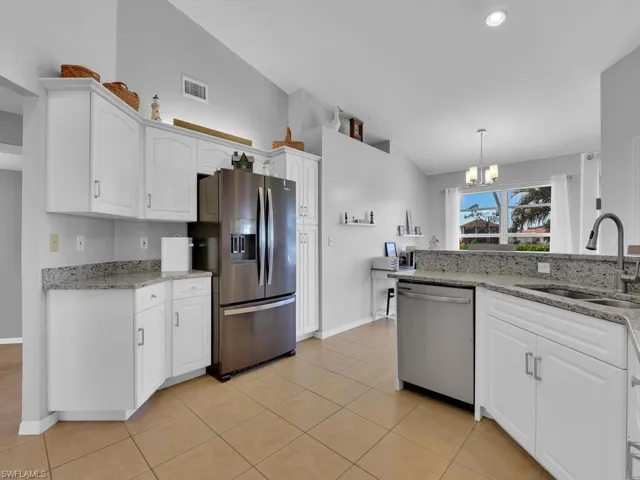 Kitchen featuring light stone counters, white cabinetry, stainless steel appliances, a chandelier, and lofted ceiling