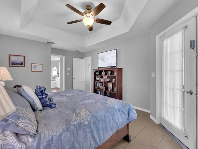 Bedroom with a tray ceiling, multiple windows, light tile patterned flooring, and a ceiling fan