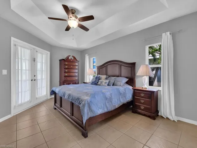 Bedroom featuring a raised ceiling, light tile patterned floors, a ceiling fan, and french doors