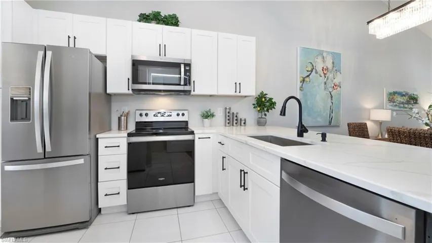 Kitchen with stainless steel appliances, white cabinets, light stone countertops, light tile patterned floors, and decorative light fixtures