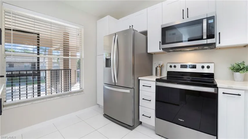 Kitchen with appliances with stainless steel finishes, white cabinetry, light tile patterned floors, and light stone countertops