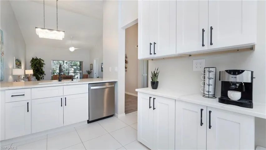 Kitchen with white cabinetry, vaulted ceiling, stainless steel dishwasher, decorative light fixtures, and light stone counters