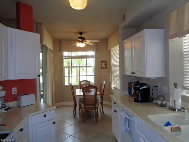 Kitchen with dishwashing machine, a ceiling fan, light tile patterned floors, light countertops, and white cabinetry