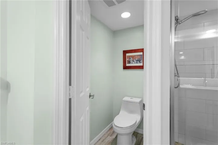 Bathroom featuring a shower with shower door, toilet, and wood-type flooring
