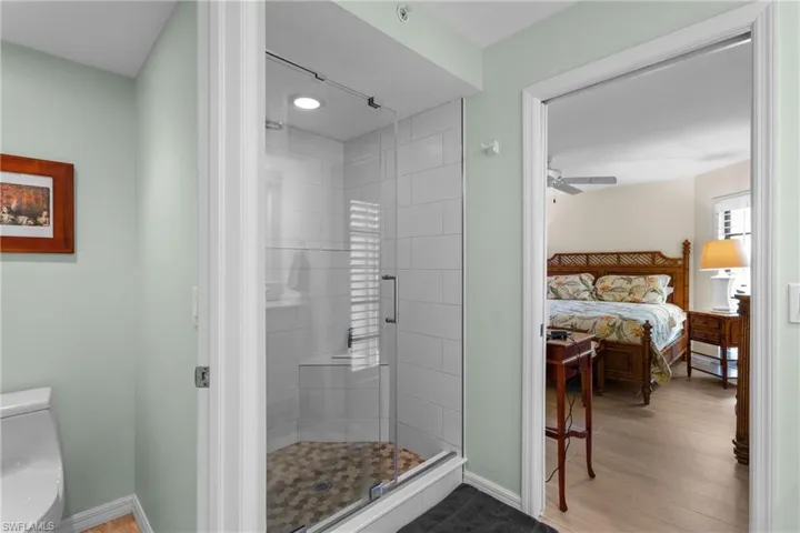 Bathroom with hardwood / wood-style flooring, toilet, an enclosed shower, and ceiling fan