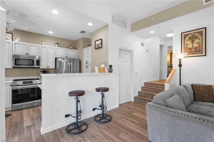 Kitchen with white cabinetry, stainless steel appliances, light hardwood / wood-style flooring, kitchen peninsula, and a kitchen bar