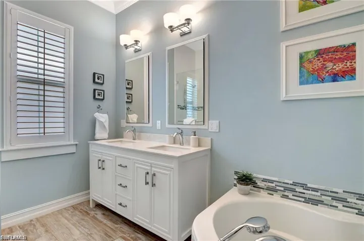 Full bath with double vanity, light wood-style flooring, and a garden tub