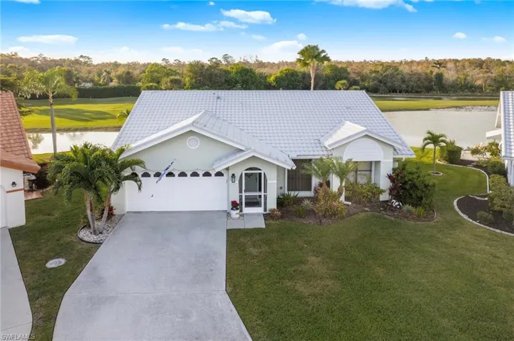 Ranch-style home with a water view, driveway, stucco siding, an attached garage, and a front lawn