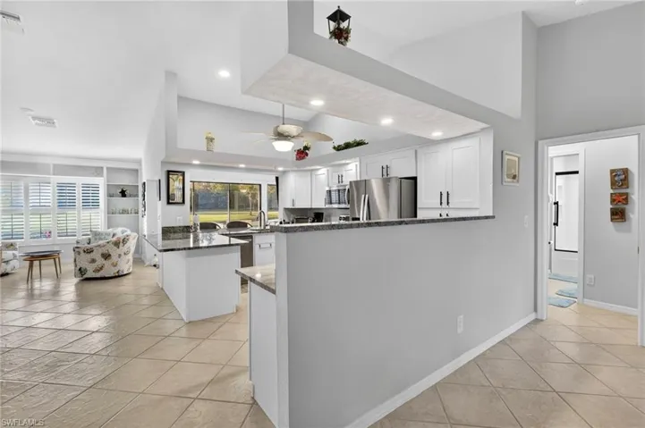 Kitchen featuring a peninsula, white cabinets, dark stone counters, appliances with stainless steel finishes, and high vaulted ceiling