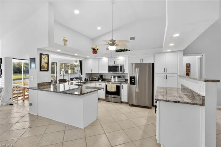 Kitchen with dark stone counters, a peninsula, a ceiling fan, stainless steel appliances, and white cabinets