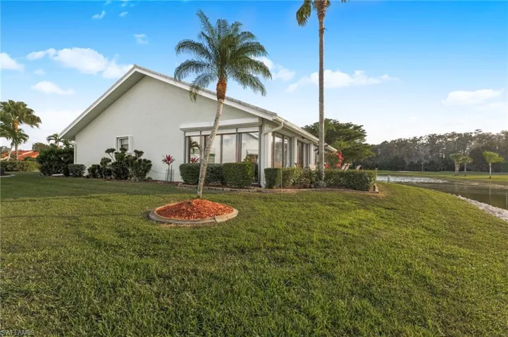 View of side of home with a sunroom, stucco siding, a yard, and a water view