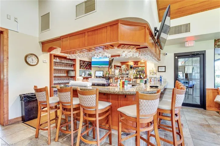 Community bar area with a high ceiling, light stone counters, brown cabinetry, and wood ceiling