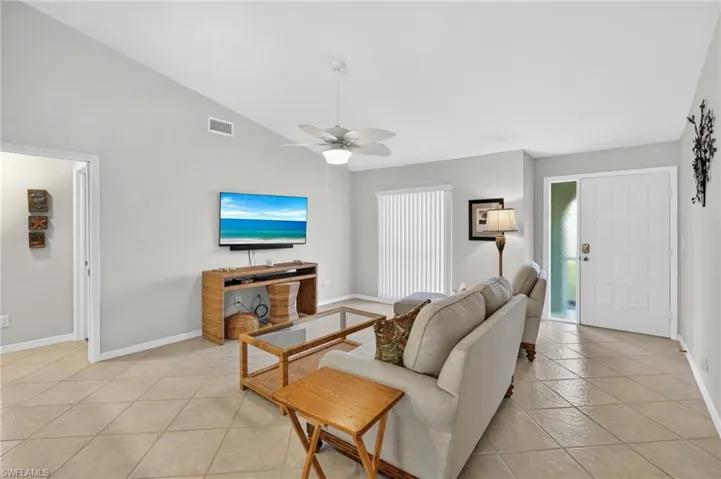Living room with lofted ceiling, a ceiling fan, and light tile patterned floors