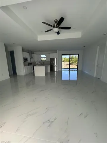 Unfurnished living room with light marble finish floors, ceiling fan, and a raised ceiling
