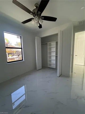 Unfurnished bedroom with marble tiled floors, a ceiling fan, and a closet