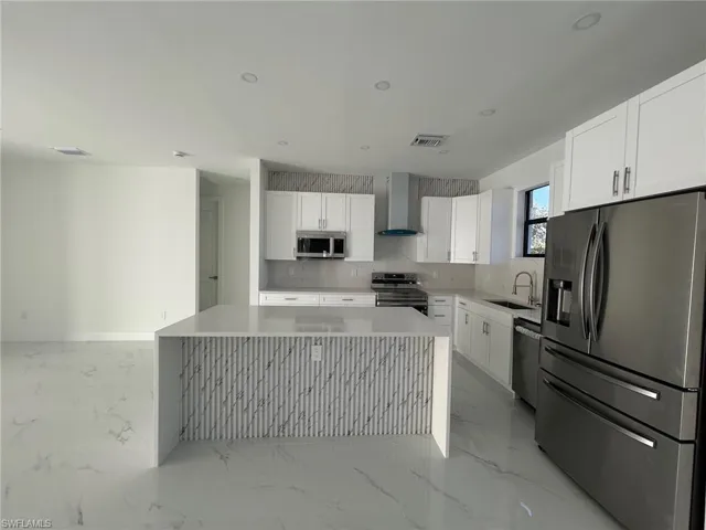 Kitchen with stainless steel appliances, white cabinets, wall chimney range hood, light stone counters, and recessed lighting
