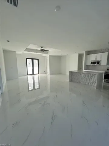 Unfurnished living room featuring a ceiling fan, light marble finish floors, and french doors