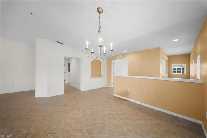 Spacious tiled area featuring a decorative chandelier, recessed lighting, an architectural niche, and multiple windows providing natural illumination