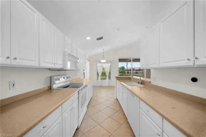 Galley kitchen featuring white cabinetry, light-toned countertops, and tile flooring
